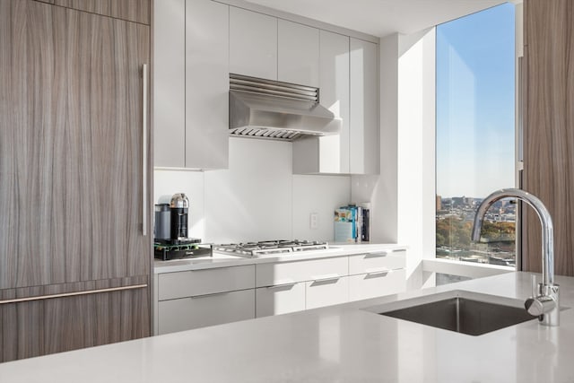 kitchen featuring stainless steel gas cooktop, white cabinetry, sink, and range hood