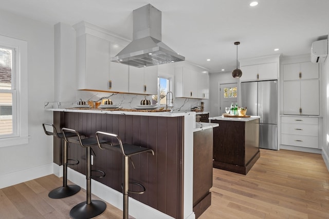 kitchen with pendant lighting, exhaust hood, light hardwood / wood-style floors, kitchen peninsula, and stainless steel refrigerator