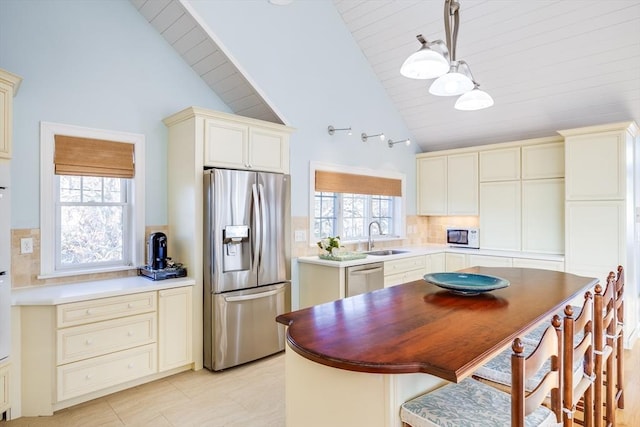 kitchen with appliances with stainless steel finishes, high vaulted ceiling, sink, decorative light fixtures, and tasteful backsplash