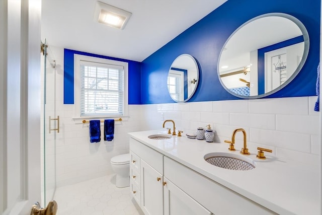 bathroom with tile patterned flooring, toilet, vanity, tile walls, and a shower with shower door