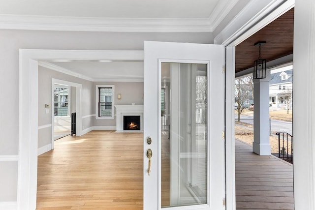 interior space with baseboards, light wood finished floors, a fireplace with flush hearth, and crown molding