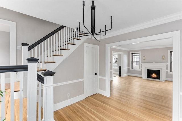 staircase with a chandelier, a fireplace with flush hearth, wood finished floors, baseboards, and crown molding