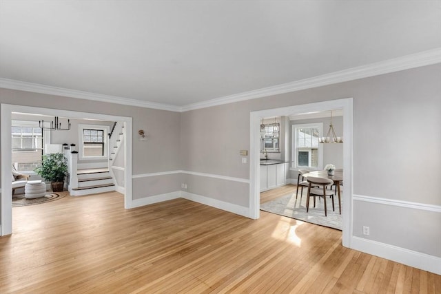 spare room featuring stairway, an inviting chandelier, ornamental molding, light wood-type flooring, and baseboards