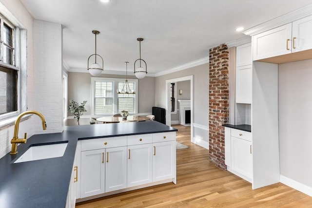 kitchen featuring a peninsula, dark countertops, a sink, and light wood-style flooring