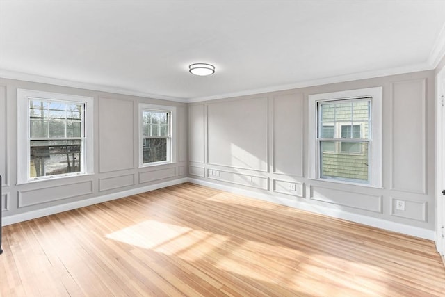 empty room featuring ornamental molding, a decorative wall, and light wood finished floors