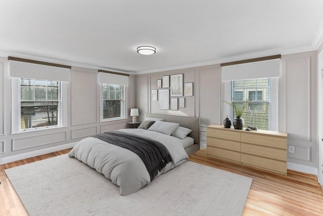 bedroom with light wood-style floors, ornamental molding, and a decorative wall