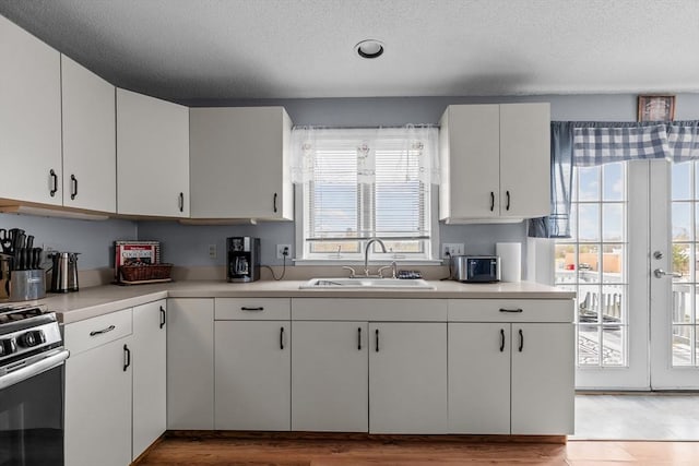 kitchen with stainless steel range with gas cooktop, a sink, light countertops, white cabinets, and a textured ceiling