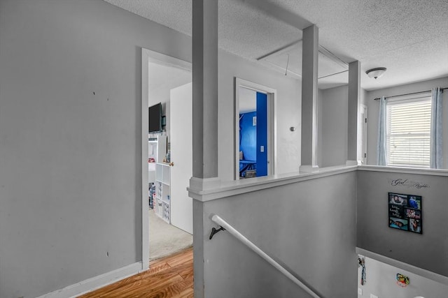 corridor featuring attic access, a textured ceiling, wood finished floors, an upstairs landing, and baseboards