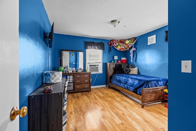 bedroom with wood finished floors, a textured ceiling, cooling unit, and baseboards