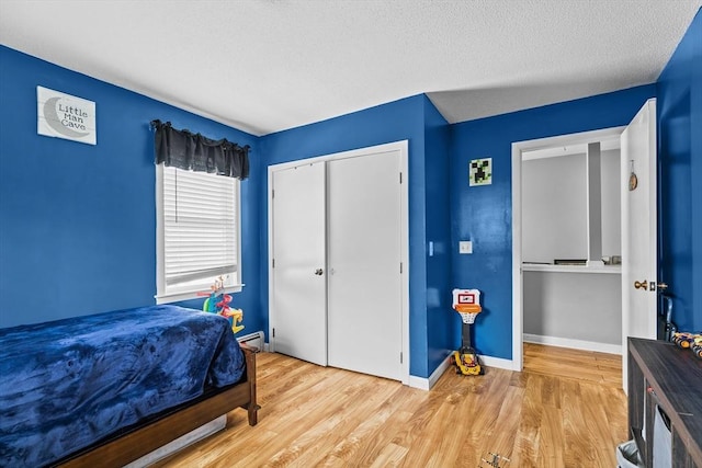 bedroom with a baseboard heating unit, light wood-style flooring, baseboards, a closet, and a textured ceiling