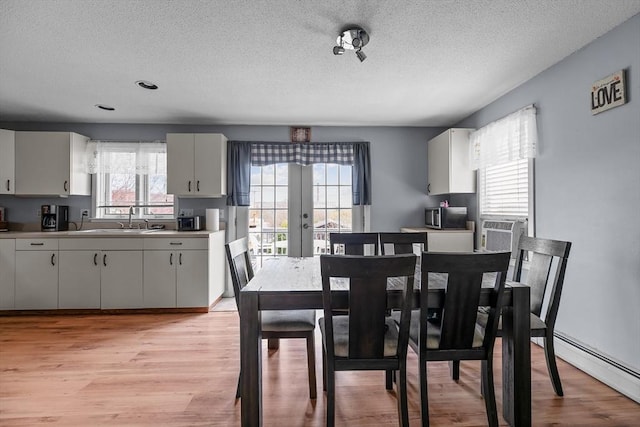 dining room with baseboard heating, a textured ceiling, french doors, and light wood-type flooring
