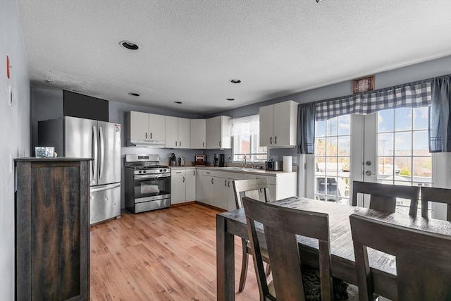 kitchen featuring appliances with stainless steel finishes, a sink, a textured ceiling, light wood-style floors, and white cabinets