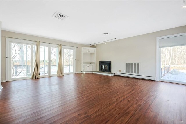 unfurnished living room featuring a wood stove, dark hardwood / wood-style flooring, a baseboard radiator, and track lighting