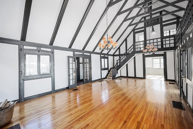 unfurnished living room with hardwood / wood-style floors, high vaulted ceiling, a notable chandelier, and beam ceiling