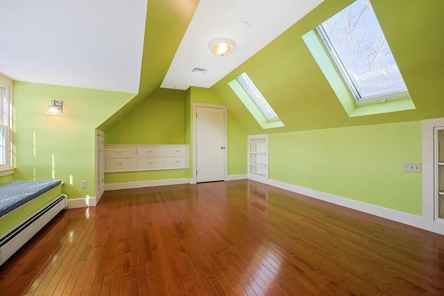 additional living space with vaulted ceiling with skylight, built in shelves, hardwood / wood-style floors, and a baseboard heating unit