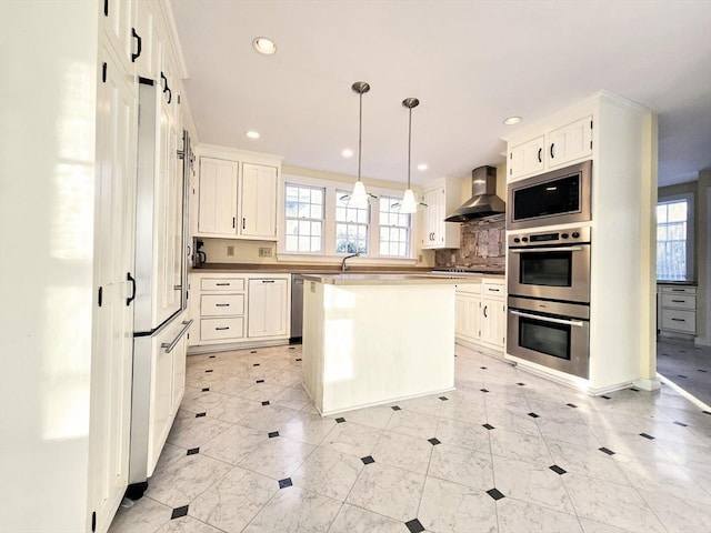 kitchen featuring appliances with stainless steel finishes, wall chimney exhaust hood, pendant lighting, white cabinets, and a kitchen island