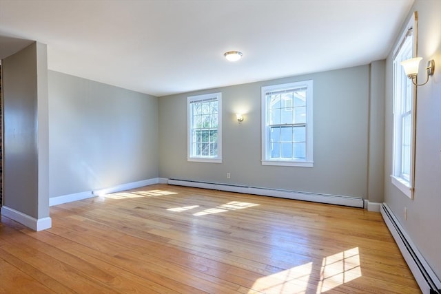 spare room with a baseboard heating unit, baseboards, and light wood-type flooring