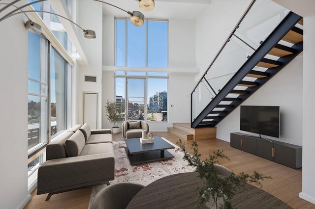living area with visible vents, a towering ceiling, wood finished floors, and stairway