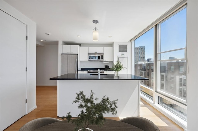 kitchen featuring dark countertops, light wood-type flooring, white cabinetry, decorative light fixtures, and stainless steel appliances