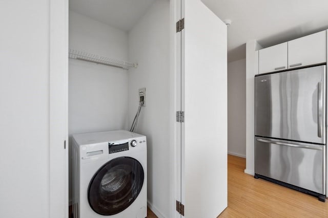 laundry area with laundry area, washer / dryer, light wood finished floors, and baseboards
