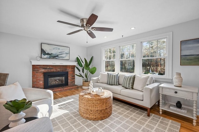 living room with hardwood / wood-style flooring, a brick fireplace, and ceiling fan