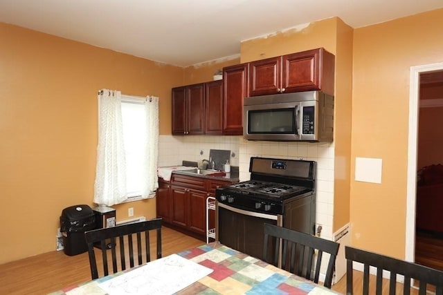 kitchen with stainless steel appliances, sink, decorative backsplash, and light hardwood / wood-style flooring