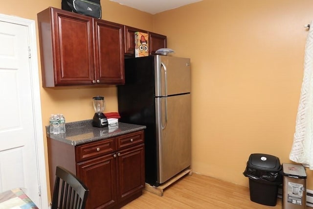 kitchen featuring dark stone countertops, stainless steel fridge, and light wood-type flooring