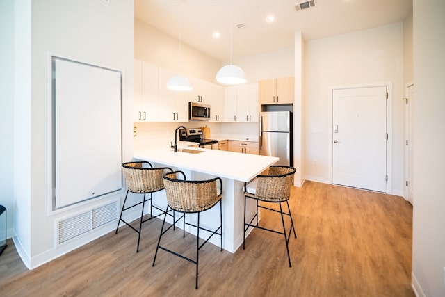 kitchen with light hardwood / wood-style floors, appliances with stainless steel finishes, a breakfast bar area, and pendant lighting