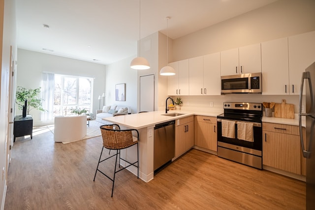 kitchen featuring kitchen peninsula, appliances with stainless steel finishes, light wood-type flooring, pendant lighting, and sink