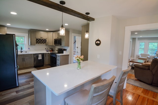 kitchen featuring a breakfast bar, dark hardwood / wood-style flooring, black appliances, hanging light fixtures, and sink