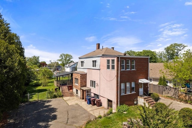 back of property featuring concrete driveway, fence, stairway, brick siding, and a chimney