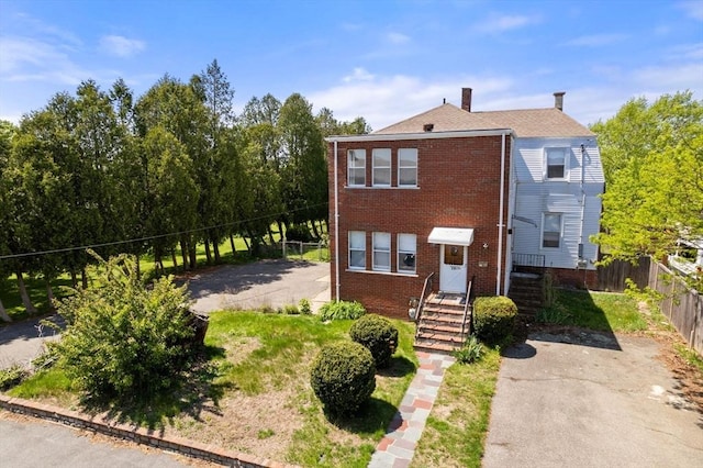 view of front of house featuring brick siding, fence, and a chimney