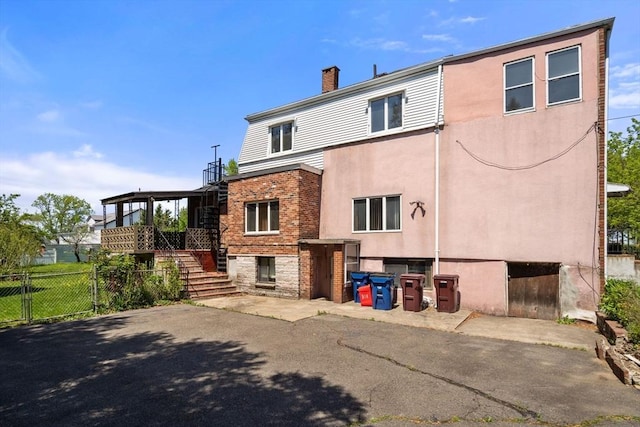 back of property featuring stairway, fence, stucco siding, and a chimney