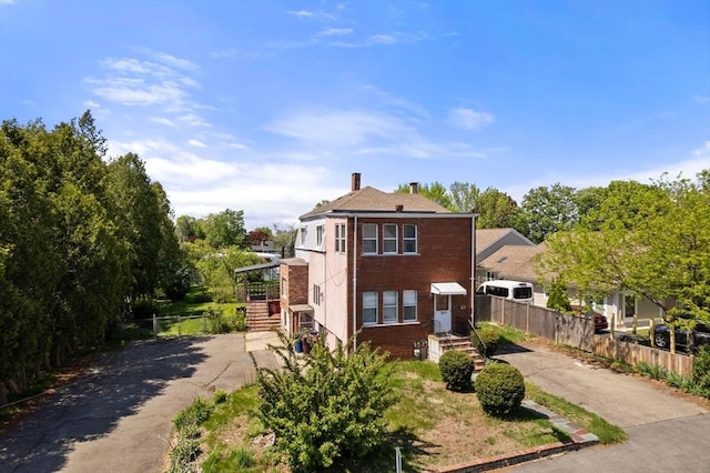 view of front of property featuring driveway, fence, brick siding, and a chimney