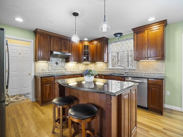 kitchen featuring pendant lighting, light wood-style floors, stainless steel appliances, and a sink