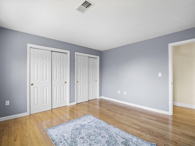 unfurnished bedroom featuring two closets, visible vents, baseboards, and wood finished floors