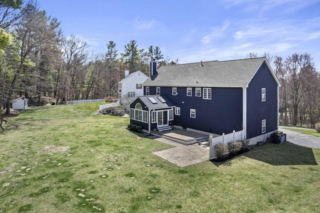 rear view of house with a chimney, a patio, a shingled roof, and a lawn