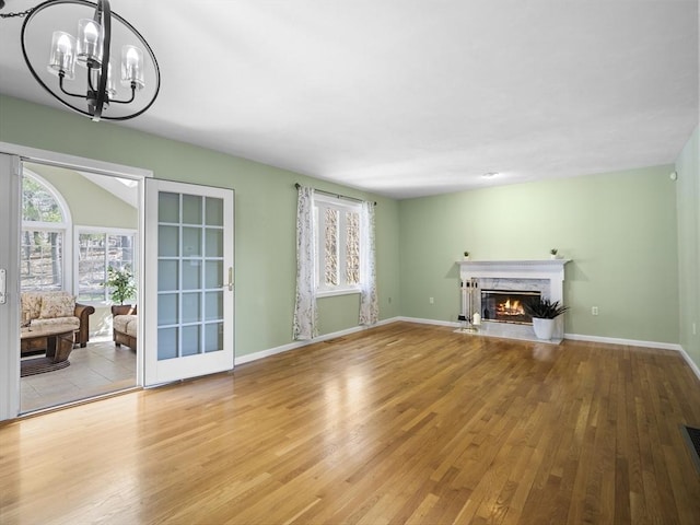 unfurnished living room featuring a high end fireplace, wood finished floors, a wealth of natural light, and an inviting chandelier