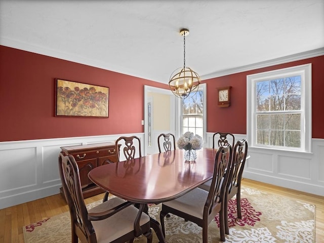 dining room featuring light wood finished floors, a wainscoted wall, a chandelier, and a decorative wall
