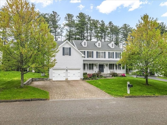 colonial inspired home with covered porch, decorative driveway, an attached garage, and a front yard