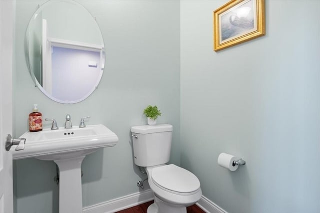 half bath with baseboards, toilet, and wood finished floors