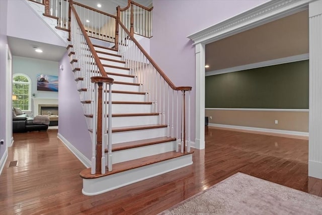 stairs featuring wood finished floors, a towering ceiling, visible vents, a fireplace, and baseboards