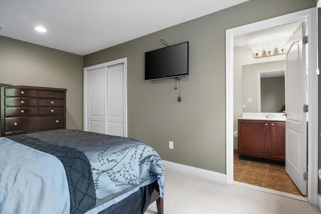 bedroom with a sink, a closet, baseboards, ensuite bath, and light carpet