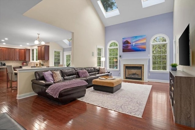 living area with a wealth of natural light, dark wood finished floors, a fireplace with flush hearth, and high vaulted ceiling