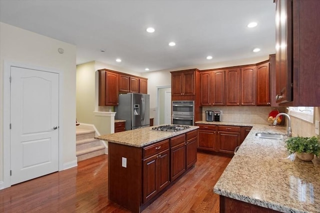 kitchen featuring a sink, wood finished floors, light stone counters, a center island, and appliances with stainless steel finishes