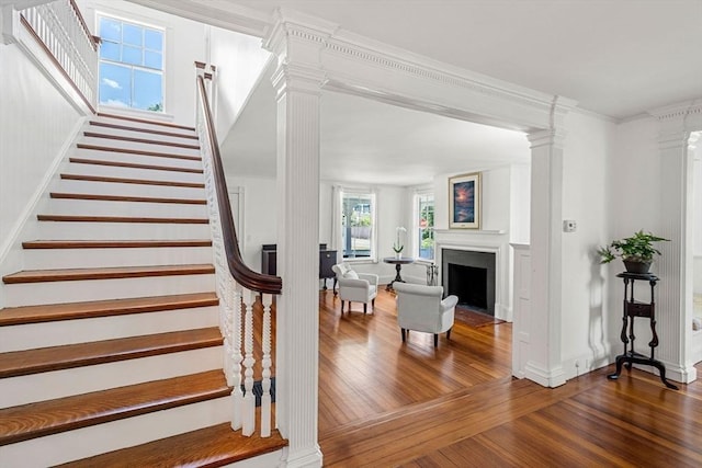 staircase featuring hardwood / wood-style flooring, crown molding, and decorative columns