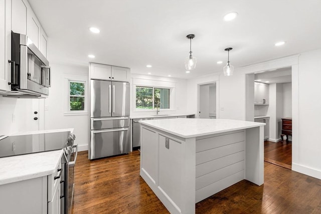 kitchen with white cabinetry, decorative light fixtures, appliances with stainless steel finishes, dark hardwood / wood-style floors, and a kitchen island