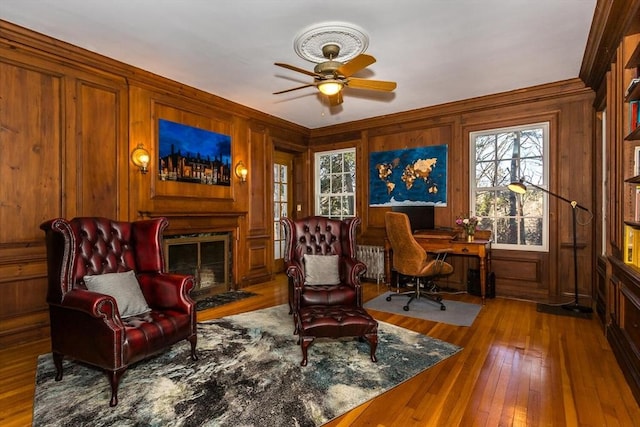 sitting room featuring wood-type flooring, a premium fireplace, ceiling fan, and wooden walls