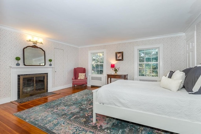 bedroom with crown molding, wood finished floors, a tiled fireplace, and wallpapered walls