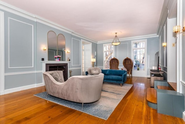 living room featuring crown molding, a fireplace, hardwood / wood-style flooring, baseboards, and a decorative wall